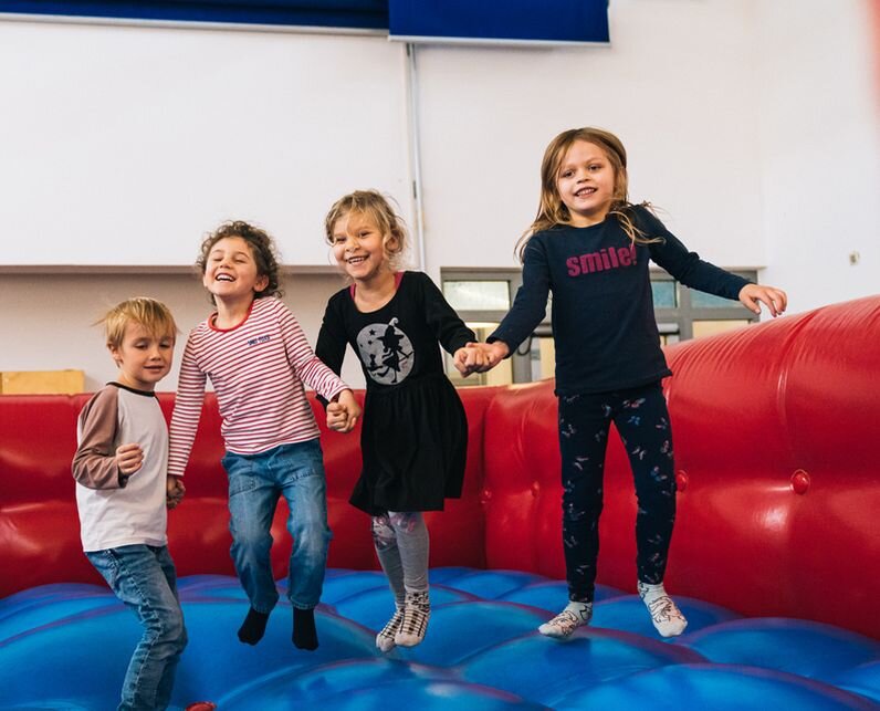 4 Kinder springen gemeinsam auf einer Hüpfburg.